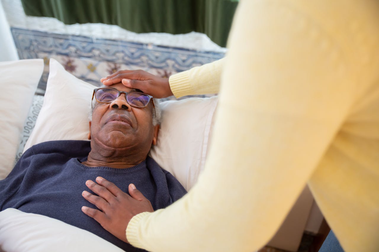 services-01 A caregiver attending to an elderly man in bed, providing comfort and support.