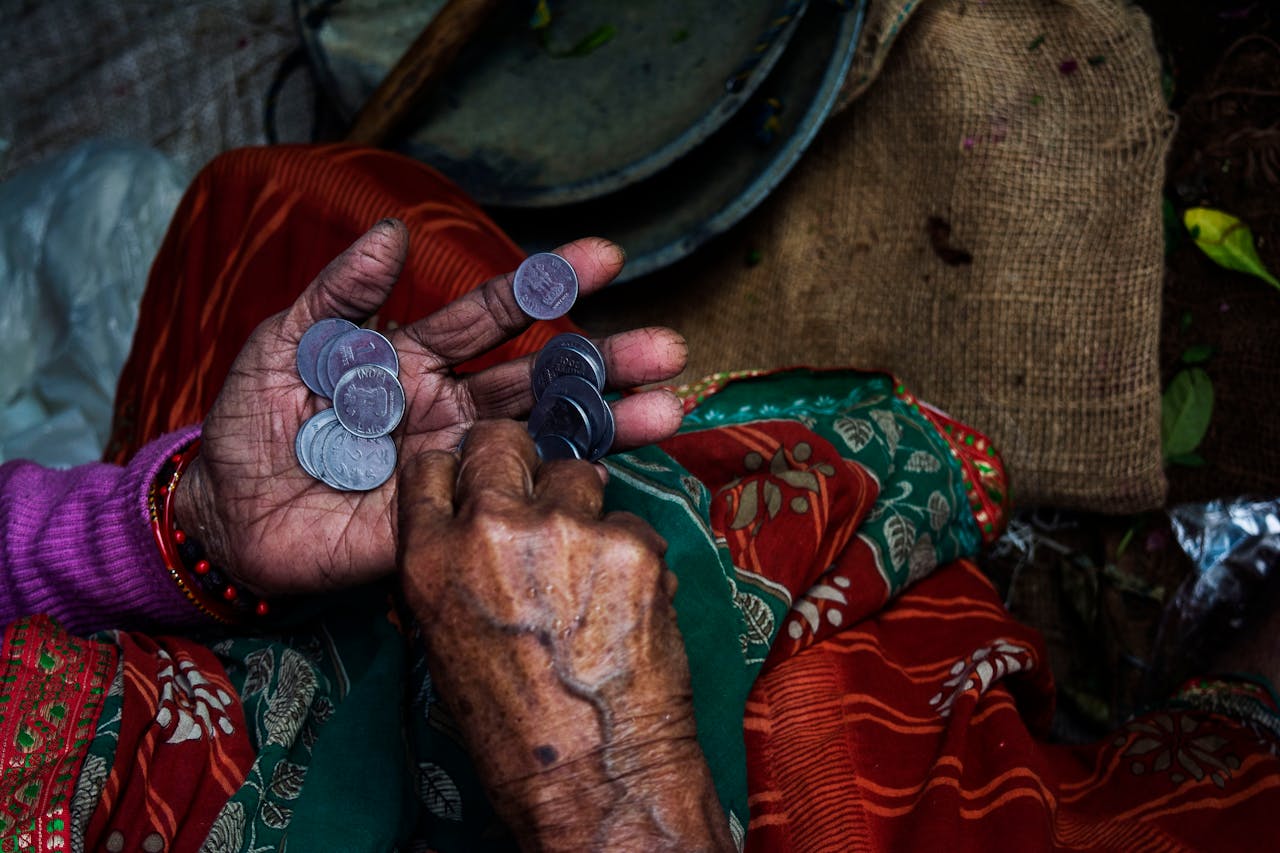 services-02 Close-up of an elderly woman's hands counting coins on a colorful textile background.